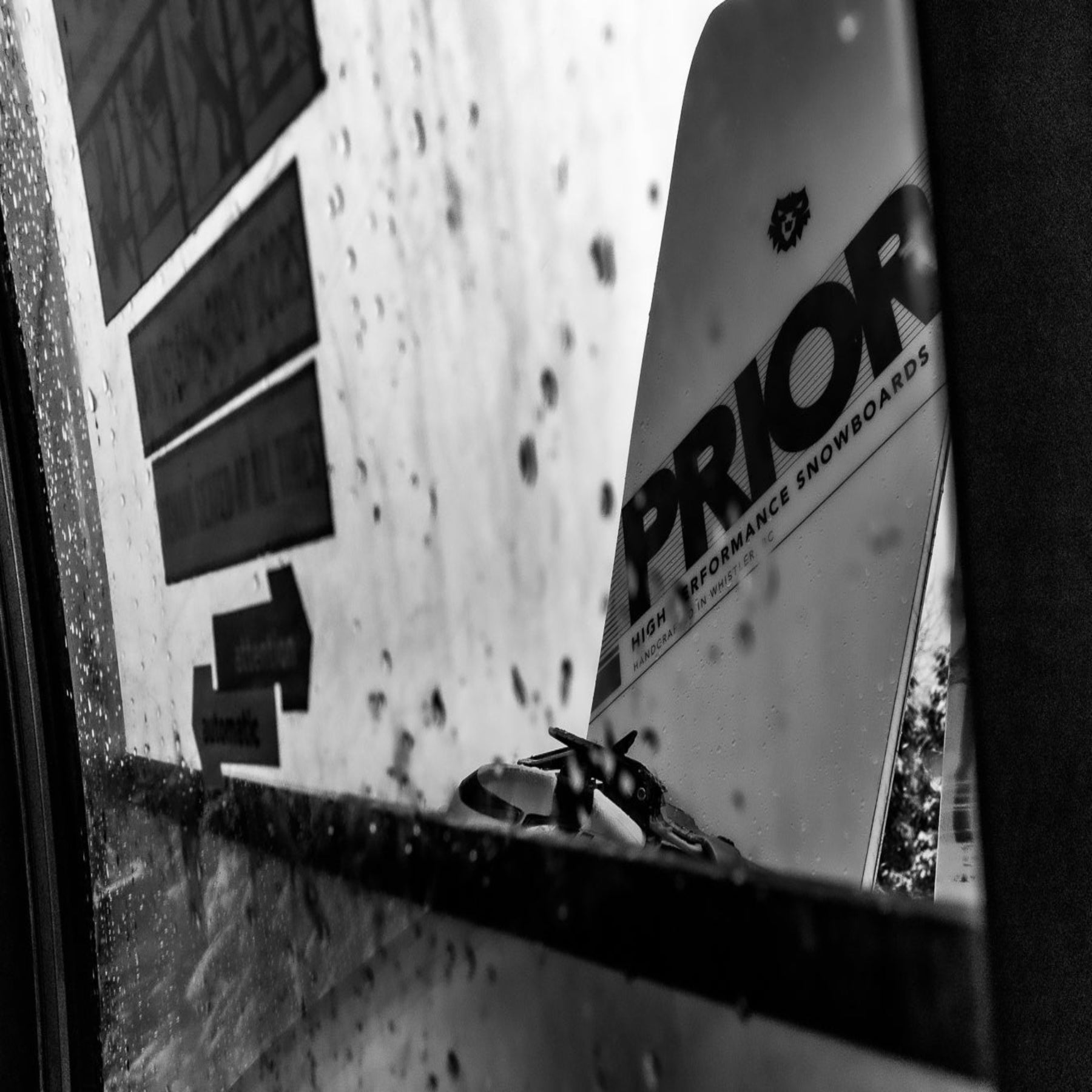 Black and white close-up of a snowboard with 'Prior' branding against a textured wall.